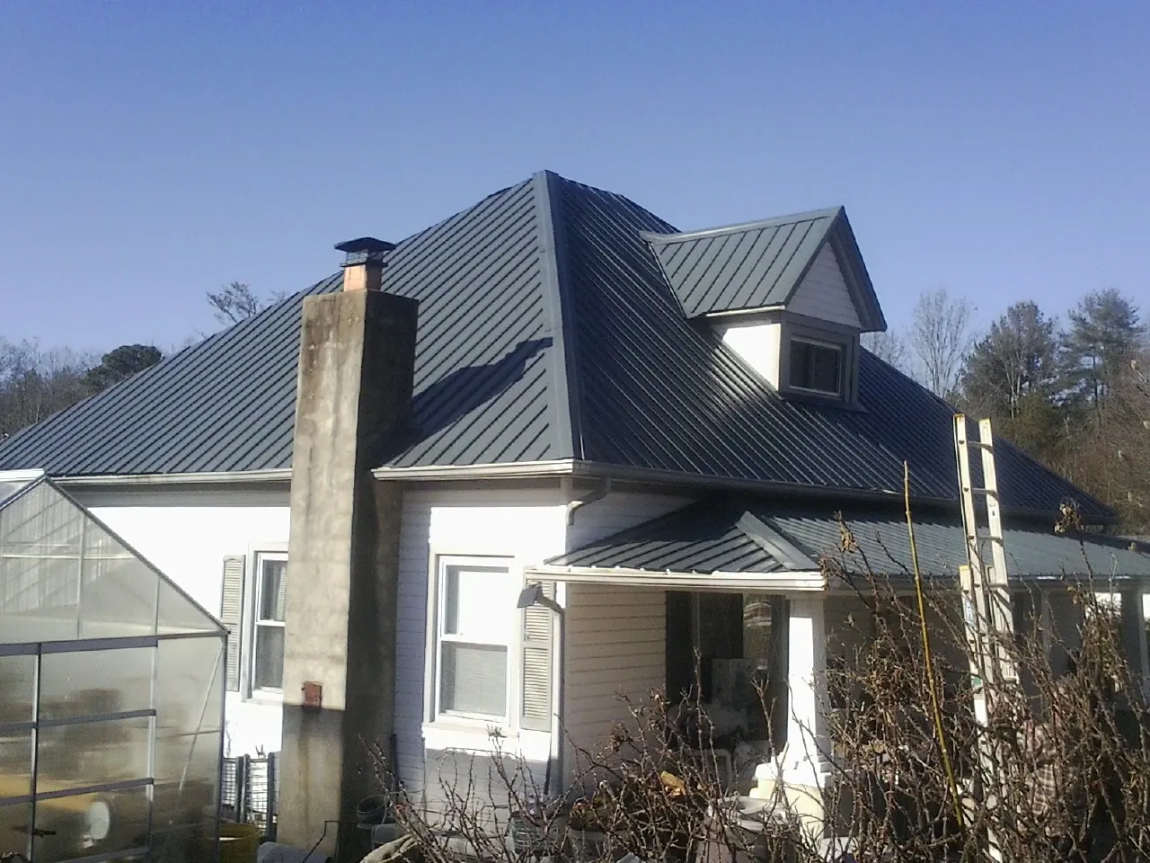 Dark blue standing seam metal roof on a white farmhouse with dormer — Slate & Tile Roof Repair by Roofing Brothers in Okatie
