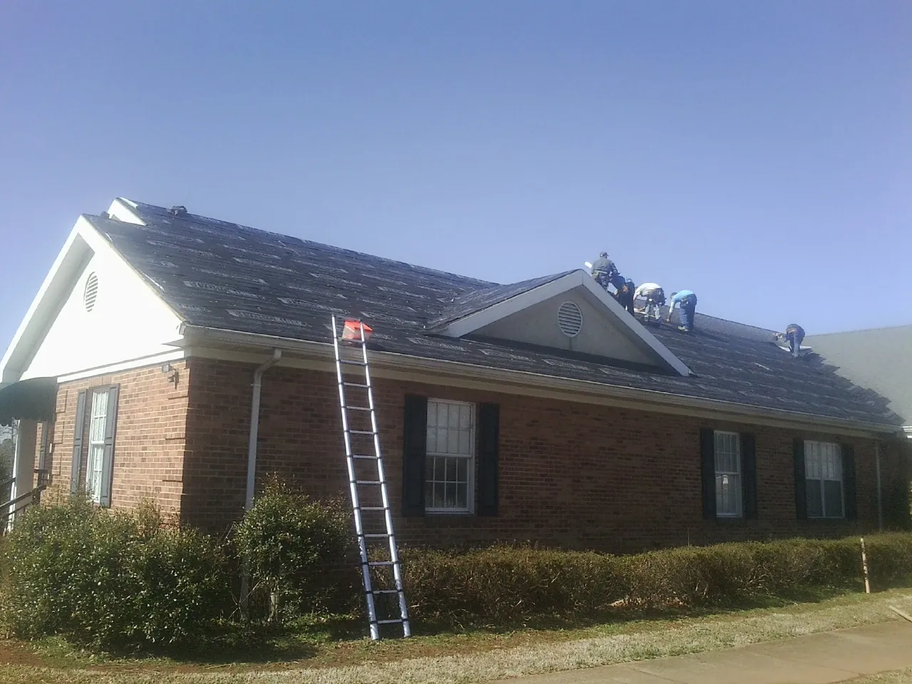 Crew tearing shingles off a brick ranch roof with a ladder set — Metal Roof Repair work by our crew in Okatie