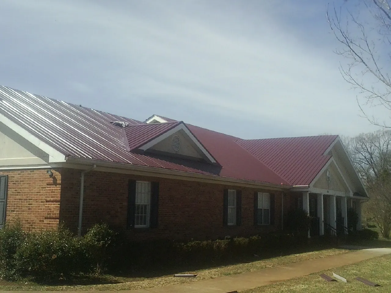Red metal roof with gabled entries on a long brick building, from a Hail Damage Roof Repair job in Okatie