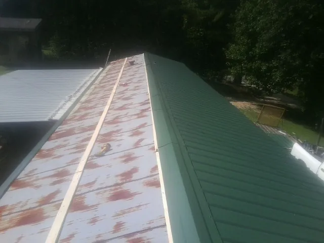 Old rusted panels beside newly installed green metal roofing — Wind Damage Roof Repair by Roofing Brothers in Okatie