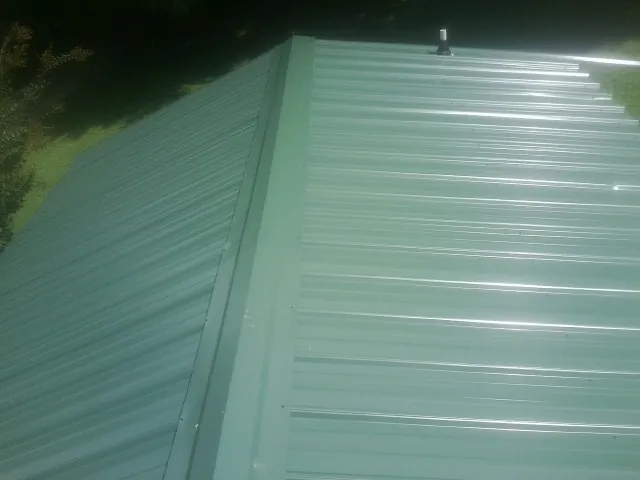 New green metal panels meeting at the ridge of a roof — Flat Roof Repair work by our crew in Okatie