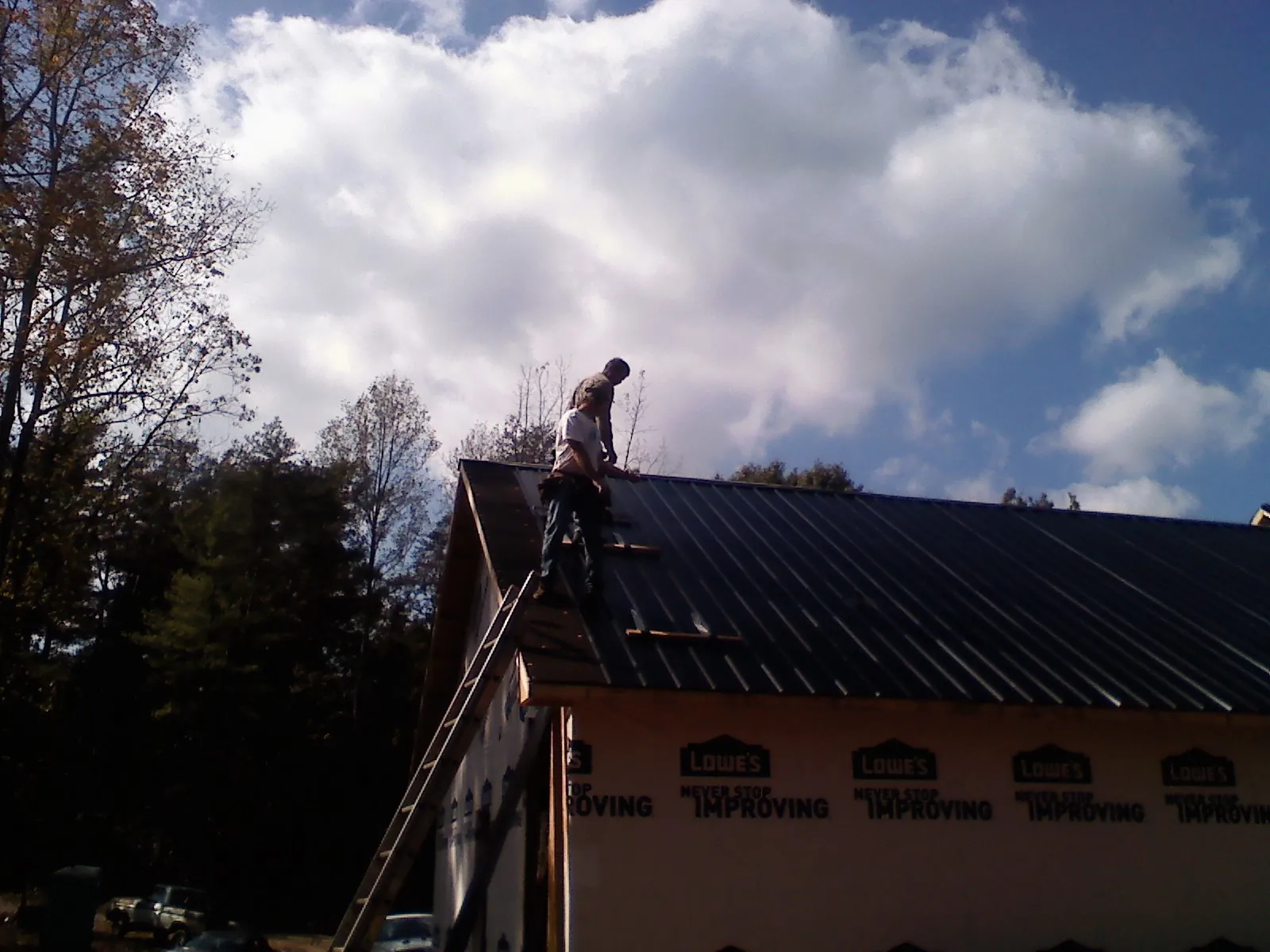 Roofer fastening dark metal panels high against a cloudy sky, from a Roof Inspection job in Okatie