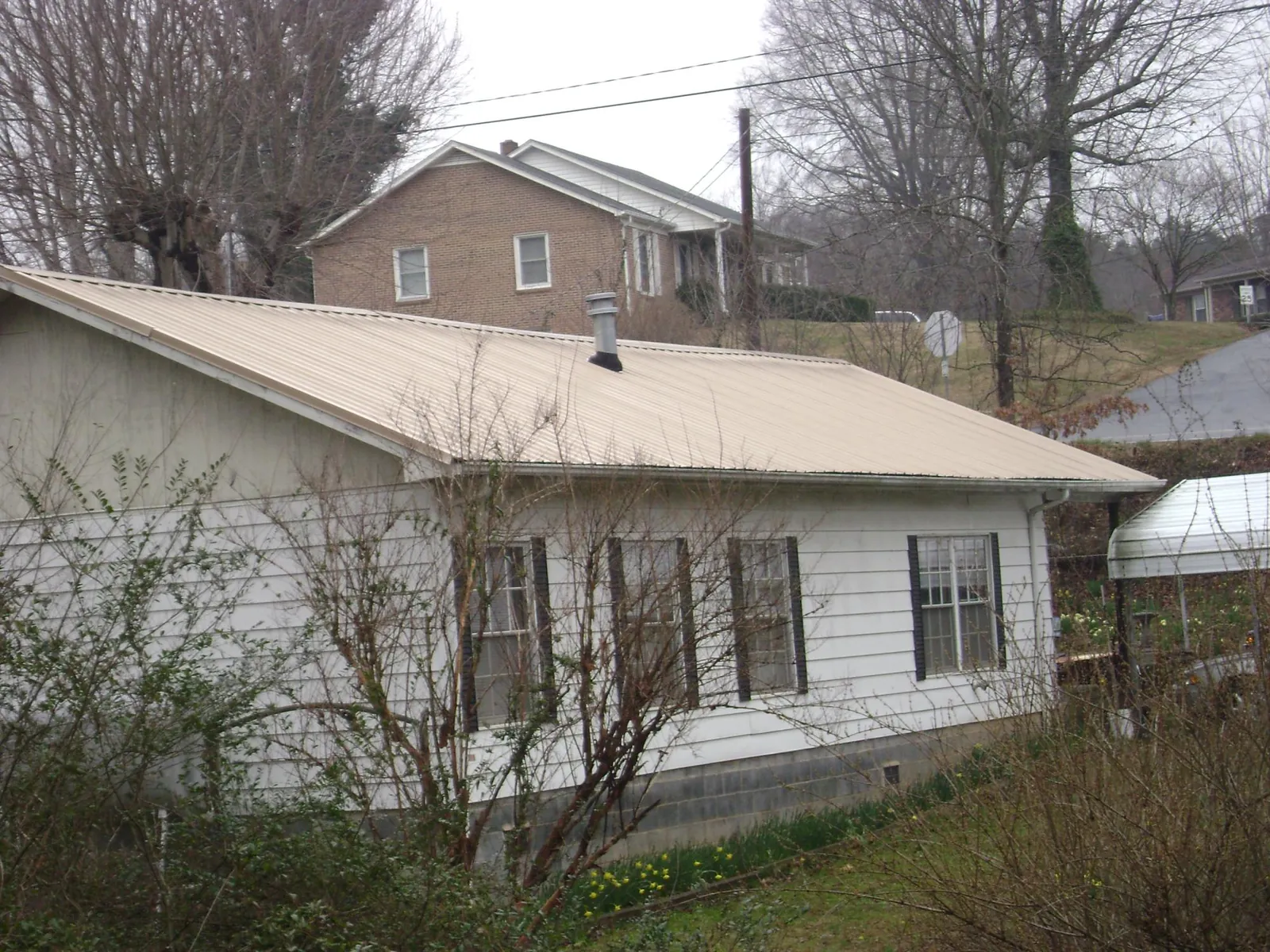 Tan metal roof on a white sided house set into a hillside — Commercial Roofing by Roofing Brothers in Okatie