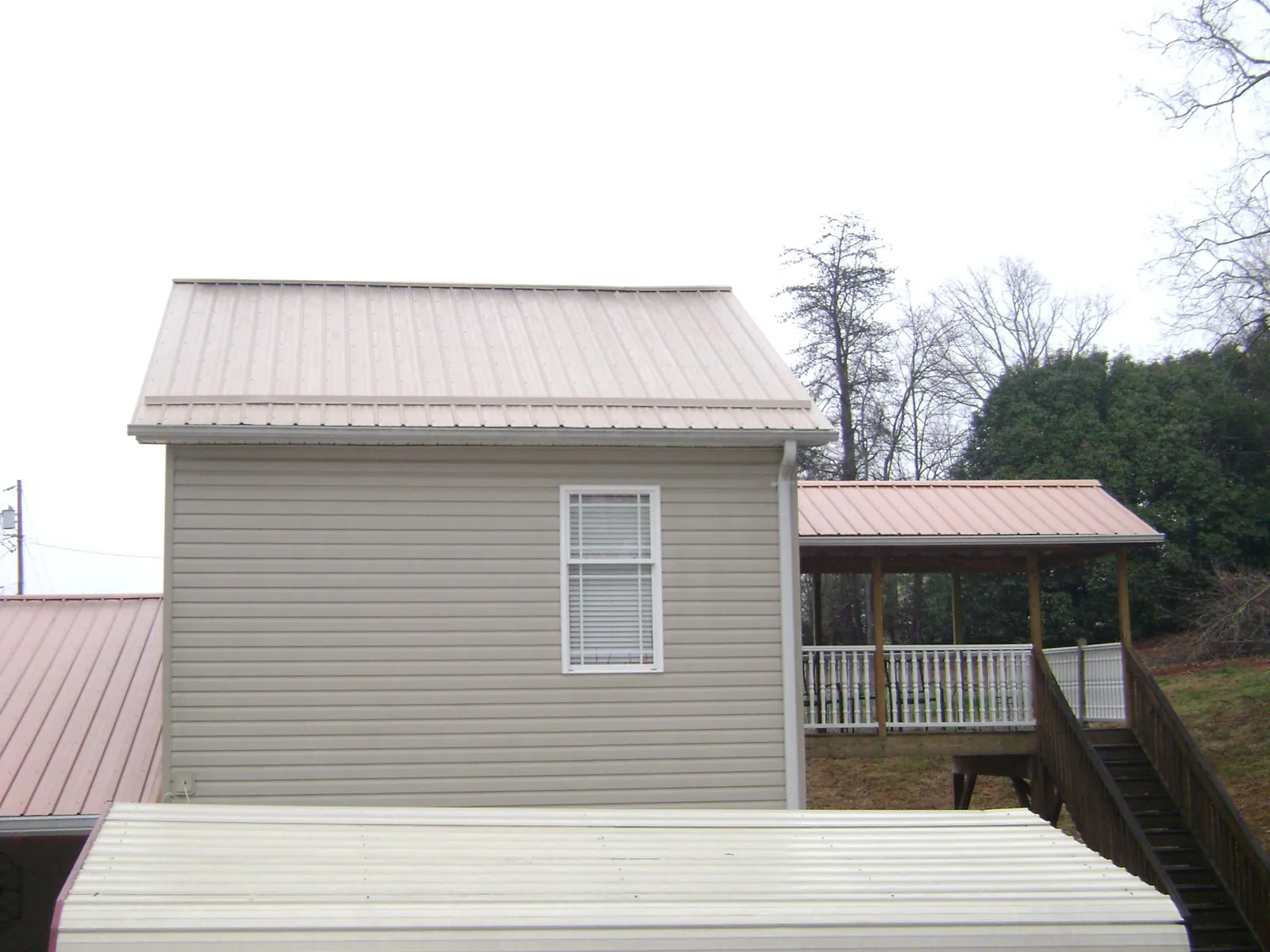 Tan metal roofs on a two story addition and attached porch, from a Roof Replacement job in Okatie